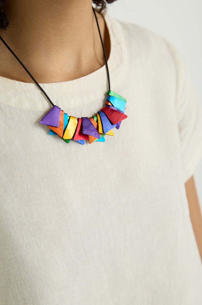 Close-up of a person wearing a cream-colored shirt and the Mini Segments Necklace—colorful, geometric-shaped beads on black cord.