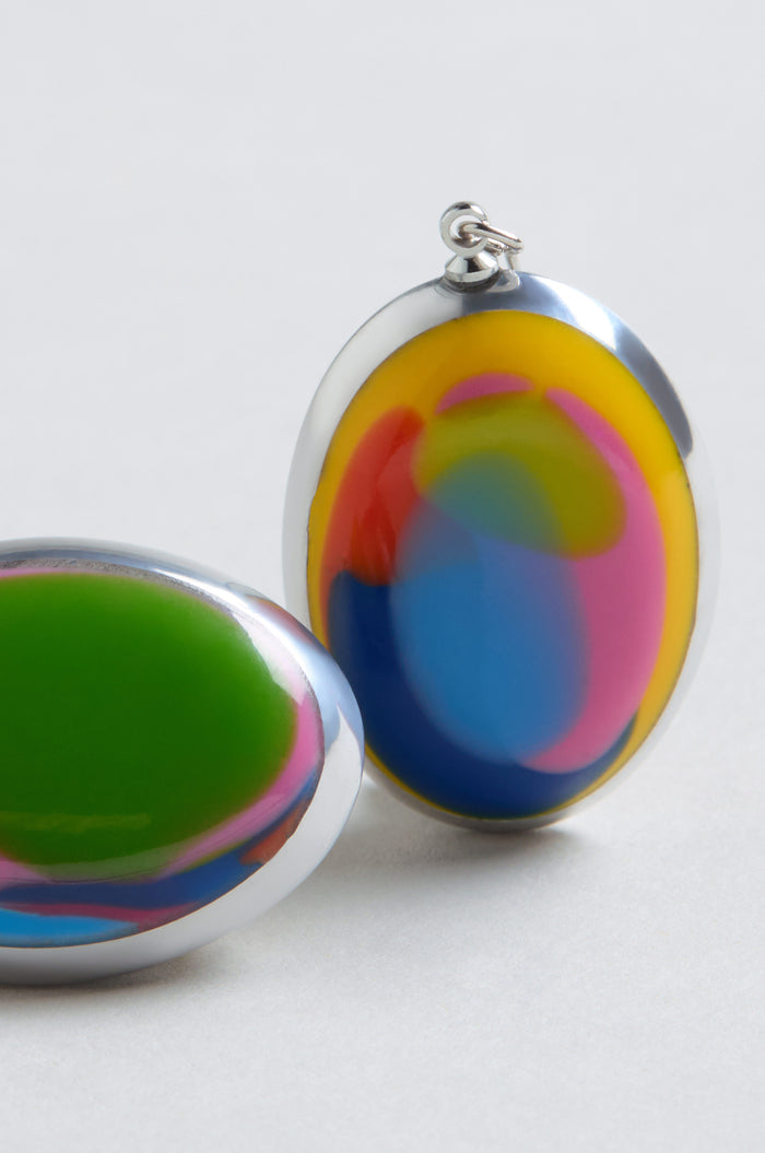 Two oval-shaped Rainbow Pebble Earrings, featuring glossy swirled patterns in green, yellow, blue, and pink, are displayed on a light gray surface.