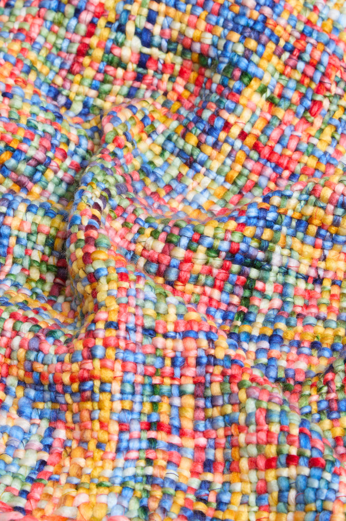 A close-up of the Rainbow Tassel Scarf highlights its colorful, textured woven fabric featuring a check pattern in blue, yellow, red, green, and pink threads, and showcases the soft brushed yarn that gives this scarf its lightweight warmth.