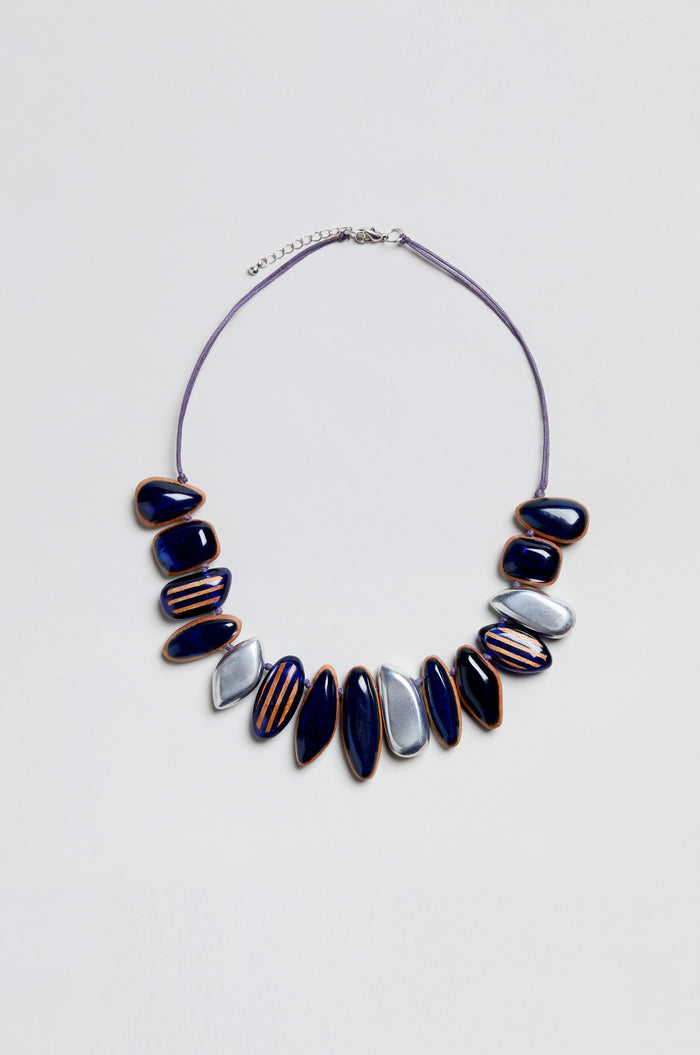 The Resin Pebble Necklace features alternating navy blue and silver oval beads—some adorned with gold detailing—arranged along a thin cord with an adjustable chain for the perfect fit, evoking the look of smooth resin pebbles.
