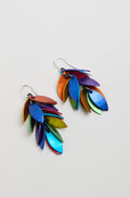 The Scattered Leaves Earrings showcase layered leaf-shaped anodised aluminium in metallic blue, green, yellow, purple, and orange, creating lightweight drop earrings that add vibrant movement to any look.