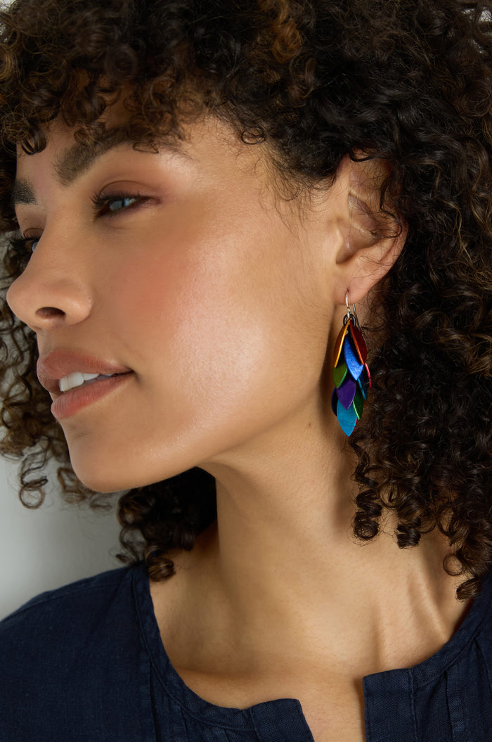 Woman with curly hair wearing a dark blue top and Scattered Leaves Earrings—lightweight, colorful drop earrings featuring layered leaf shapes in anodised aluminium.