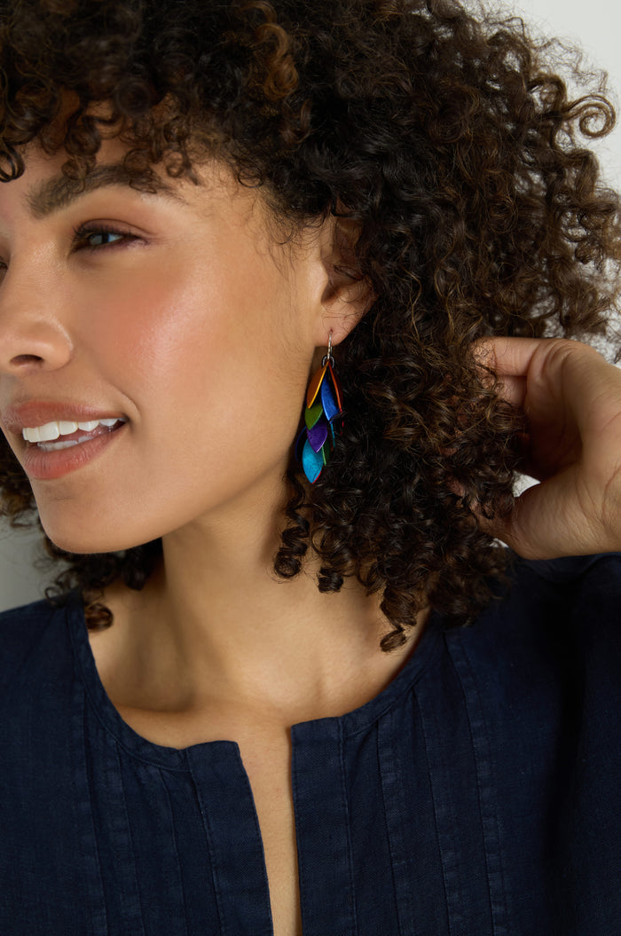 A person with curly hair, turned to the side, wears colorful and lightweight Scattered Leaves Earrings made of anodised aluminium and a navy blue top.