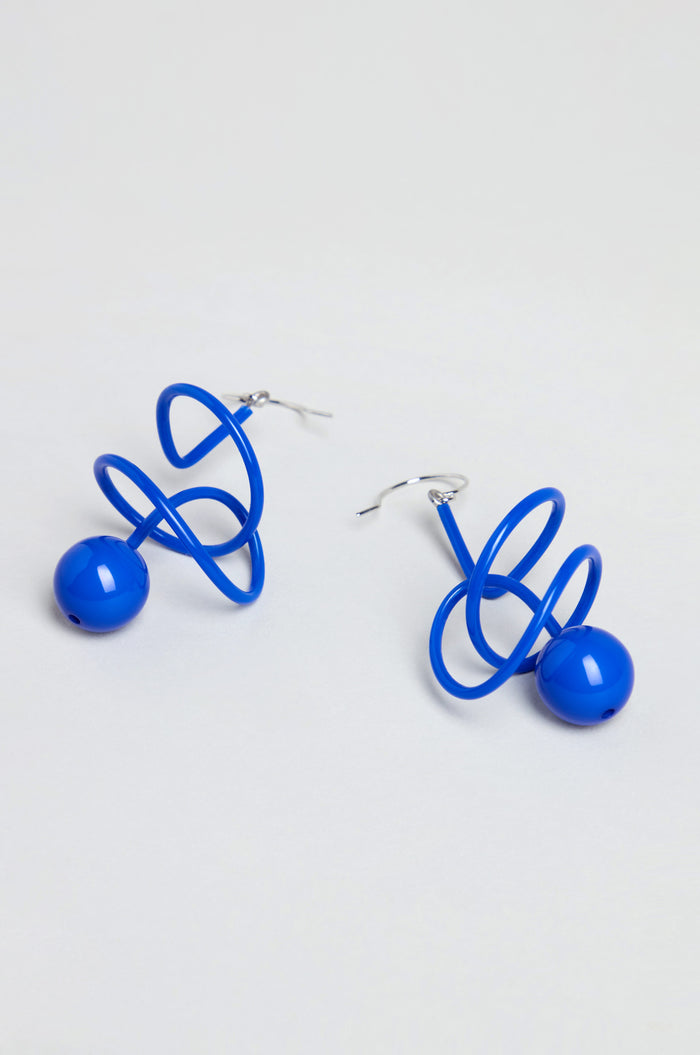 The Scribble Sphere Earrings, handmade in Paris, feature a sculptural blue spiral wire with a round bead at the base and are shown on a plain white background.