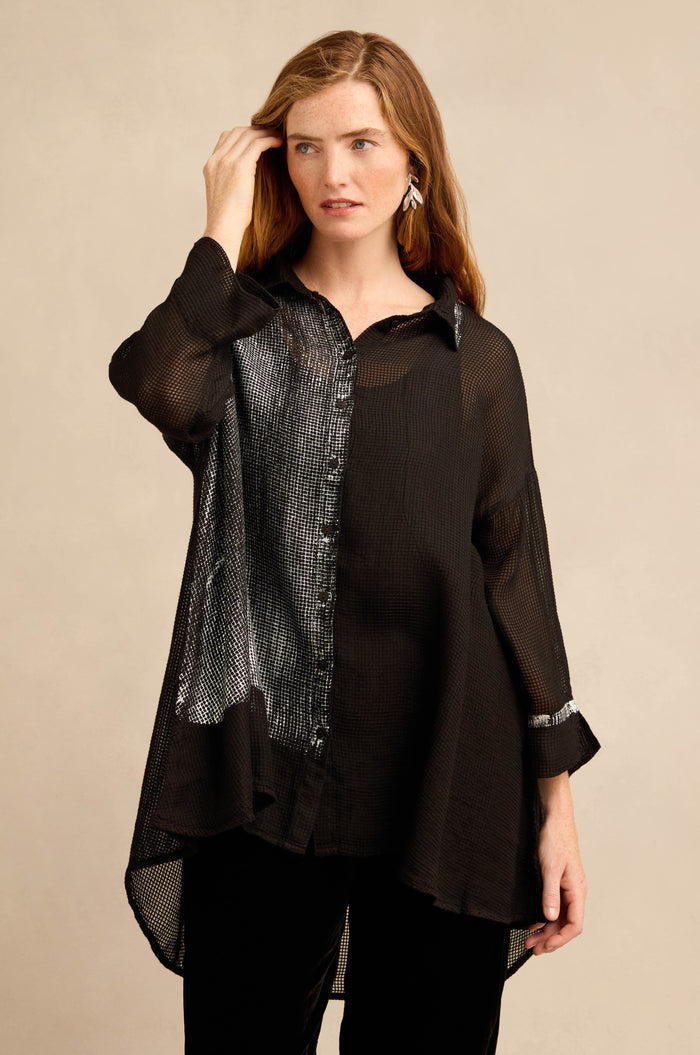 A woman wears the Sheer Silver Panel Flared Shirt—an airy, loose-fitting blouse with metallic silver panels and shiny accents—standing against a plain beige background.