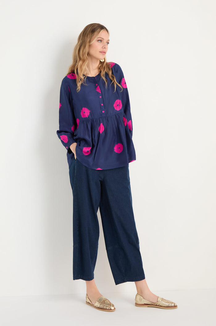 A woman stands against a white background wearing the Shibori Spot Silk Shirt, paired with wide-leg cropped jeans and metallic loafers. She has her hands in her pockets and is looking to the side.