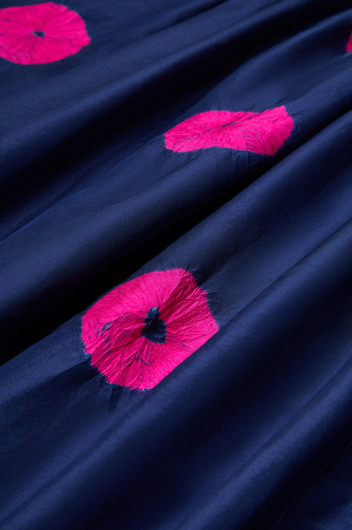Close-up of the Shibori Spot Silk Shirt, featuring dark blue artisanal fabric with irregular bright pink circles. The slightly wrinkled, shiny material evokes classic Shibori patterns on luxurious silk.