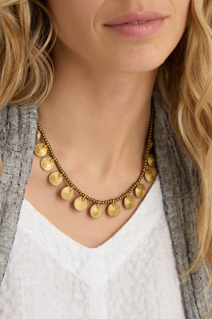 A woman wearing a textured gray jacket, a white V-neck top, and the Short Gold Chakra Necklace.