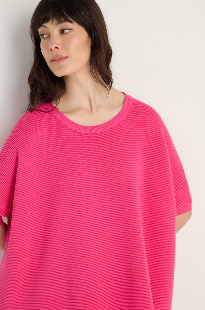 A woman with long dark hair wears the Short Sleeve Hot Pink Ribbed Top and stands against a plain light-colored background.