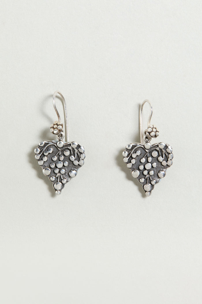 Add a delicate touch to any look with the Silver Heart Earrings—sterling silver drop earrings featuring heart shapes with floral and dot details, perfect against a light background.