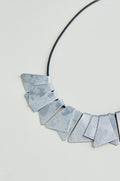 The Mini Segments Necklace features a black cord with textured silver triangular segments arranged in a row, creating a modern geometric jewelry look.