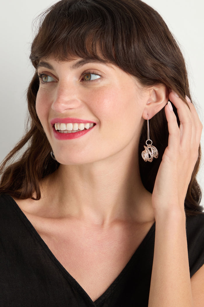 A woman with brown hair smiles and touches her Silver Scribble Earrings. She wears a black top and looks to the side, highlighting the lightweight, contemporary design of the earrings.