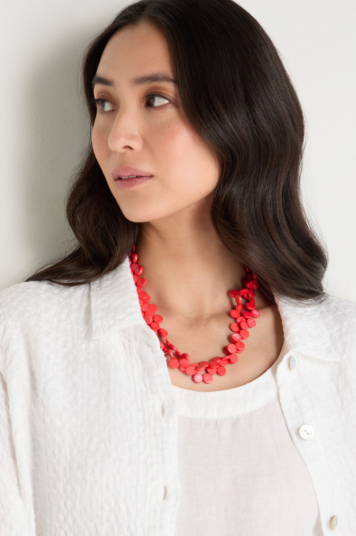 Woman with long dark hair wears a white textured top and the Single Strand Coco Necklace—a handcrafted red beaded accessory—while looking to the side against a light background.