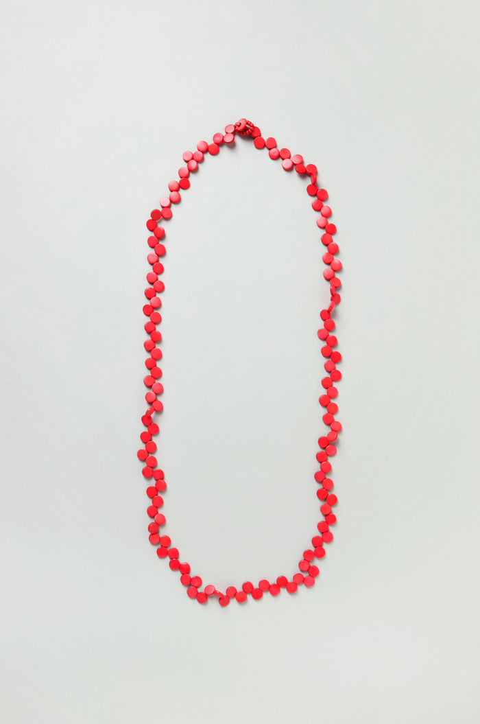 The Single Strand Coco Necklace is a handcrafted piece made from coconut shell, featuring red beads in an oval design on a plain light background.