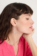 A woman with short brown hair rests her chin on her hand, wearing a bright pink textured top and Sketch Ball Earrings—large, sculptural accessories that appear handmade in Paris—against a plain background.