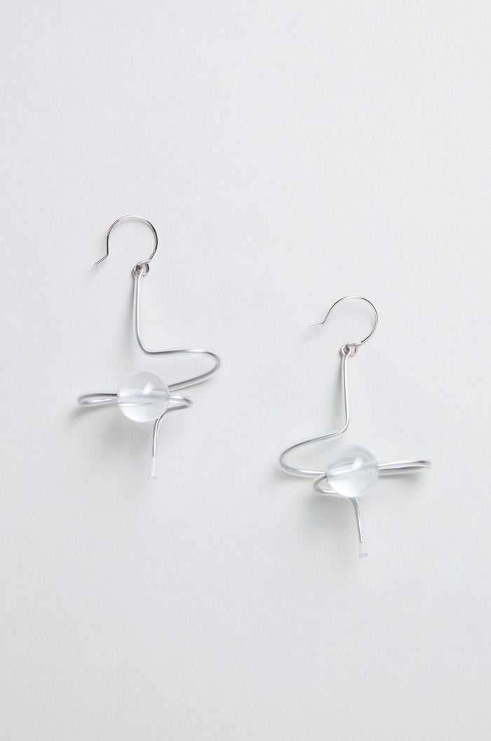 The Sketch Ball Earrings are handmade in Paris, featuring a silver sculptural form with abstract swirling shapes and a clear round bead at the center.