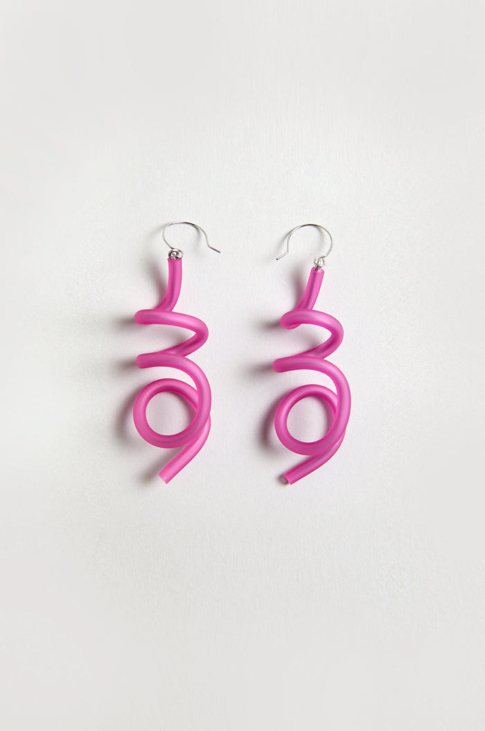 The Sketch Earrings feature bright fuchsia tubing twisted into abstract spiral shapes, creating a sculptural form. Displayed on a plain white background.