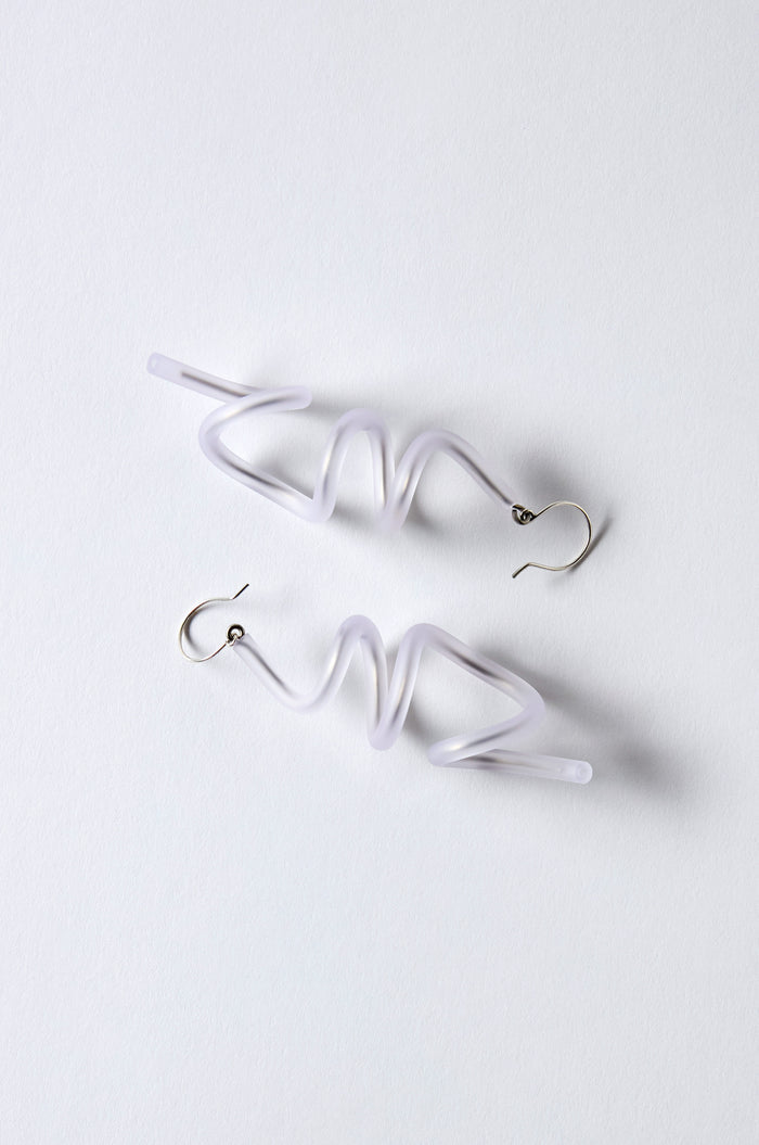 The Sketch Earrings feature silver hooks and irregular, zigzag-shaped translucent white rubber bodies reminiscent of Samuel Coraux's sculptural spiral style, displayed on a white background. Lightweight and bold, they highlight creative design.