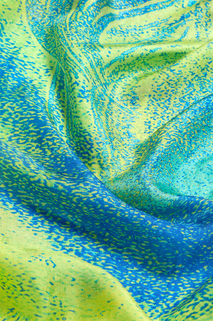 Close-up of the Sky Dance Silk Scarf, featuring blue and yellow abstract patterns like a topographic map, highlighting its folds, texture, and fluid drape.