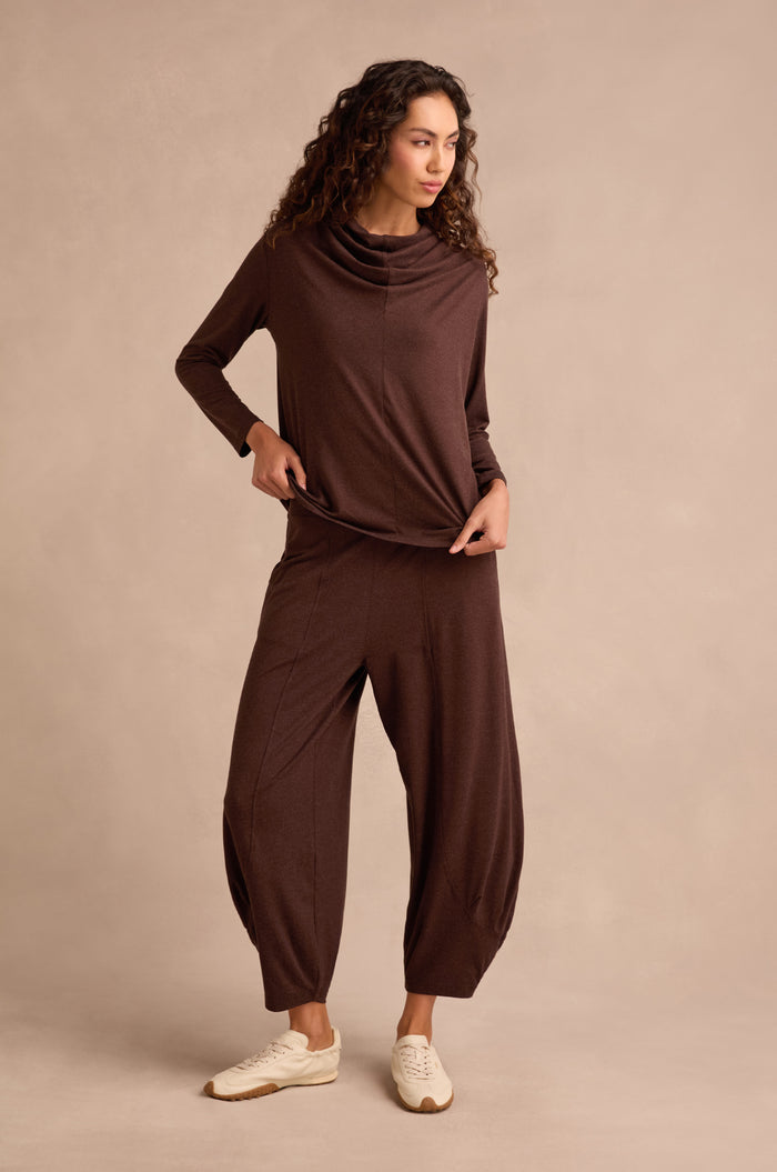 A woman stands against a beige background wearing the Soft Viscose Jersey Ruched Top in brown, paired with matching wide-leg pants and white sneakers.