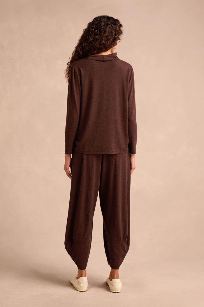 Person standing against a plain background, wearing the Soft Viscose Jersey Ruched Top in brown—a loose-fitting, long-sleeve cowl neck style—paired with matching wide-leg pants and white sneakers, facing away from the camera.