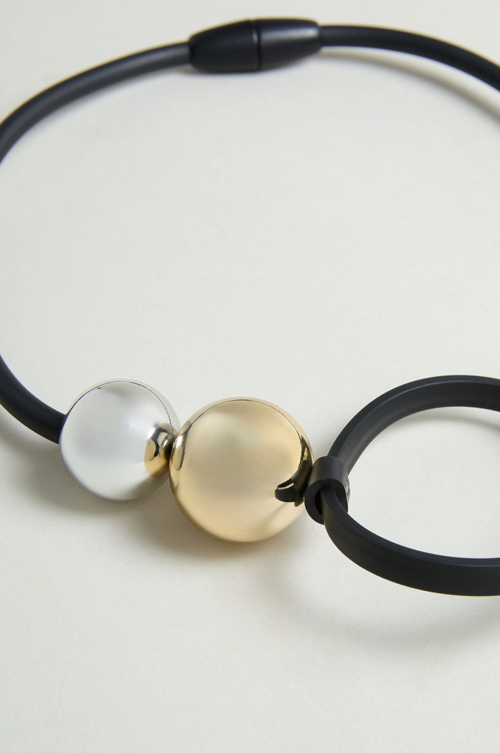 The Space Necklace features a matte black design with one silver and one gold metallic round bead at the center, accented by oversized acrylic beads for a bold statement.