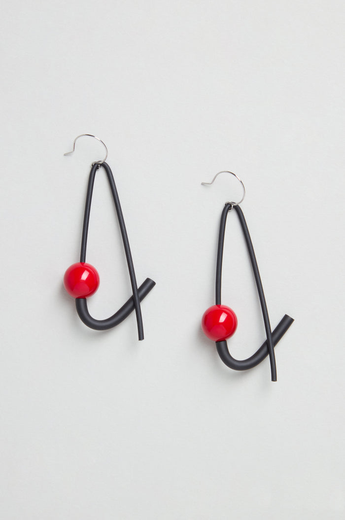 Sphere Earrings: Modern sculptural earrings handmade in Paris, each featuring black curved wire and a red spherical bead, displayed on a light background.