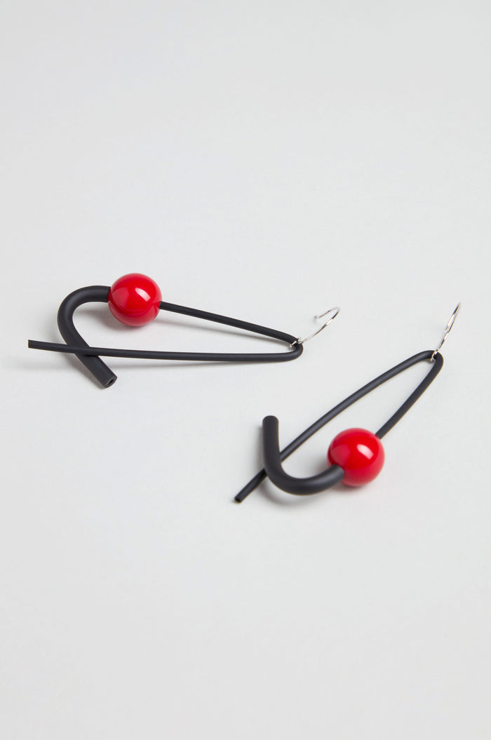 The Sphere Earrings are handmade in Paris, featuring sculptural geometric shapes crafted from black metal wire and accented with a vibrant red spherical bead.