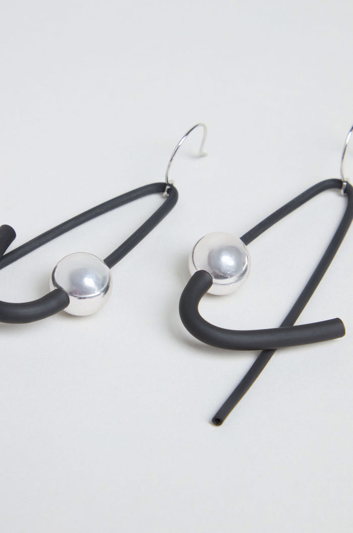 The Sphere Earrings are a pair of contemporary, handmade earrings from Paris featuring black rubber loops, silver-tone spherical beads, and metal hooks, elegantly displayed on a light background.