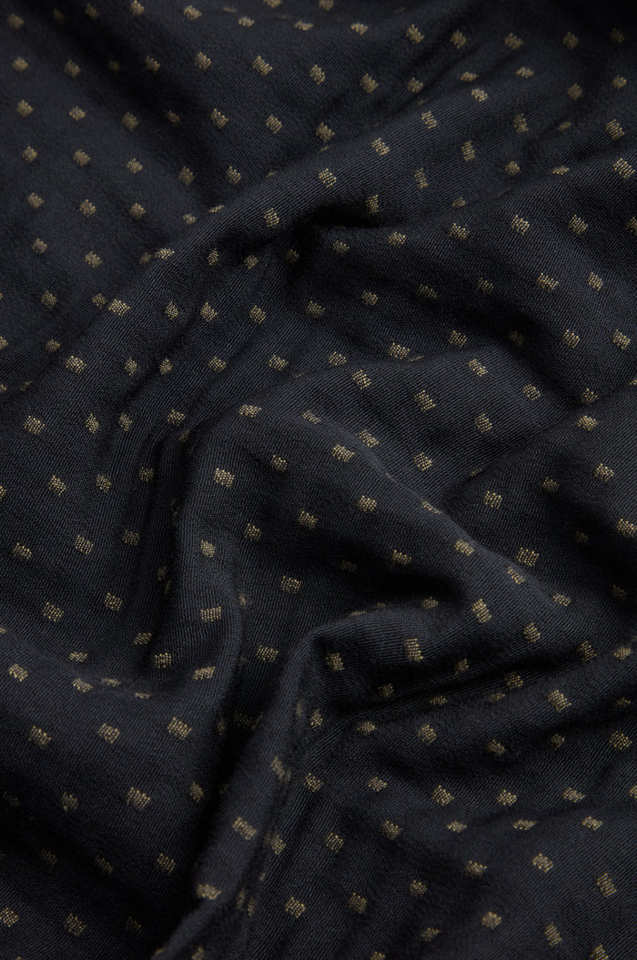 Close-up of the Square Jacquard Bubble Trousers showcasing black fabric adorned with a subtle grid of small, evenly spaced gold dots. The cotton-rich blend appears soft and slightly wrinkled, highlighting the luxurious texture characteristic of this sophisticated design.