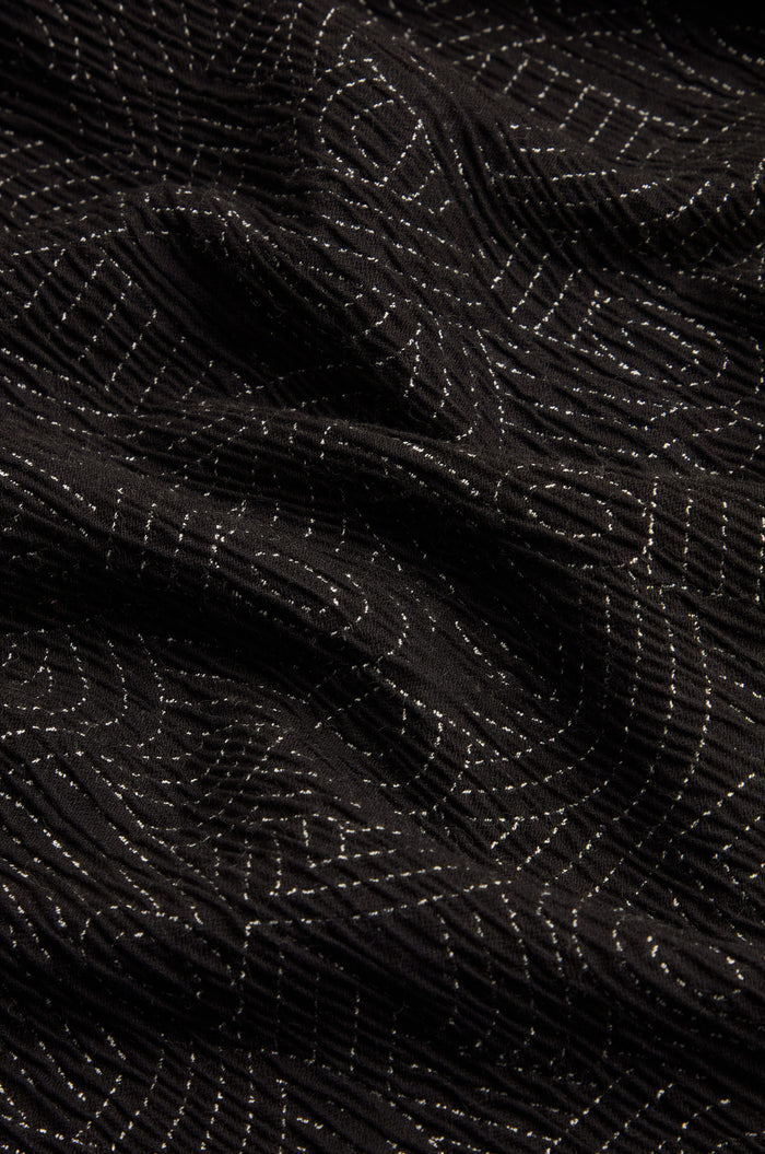 Close-up of black fabric with undulating folds, featuring thin, white, horizontal and curved stitched lines that echo the intricate detailing of the Stitched Jacquard Jacket.