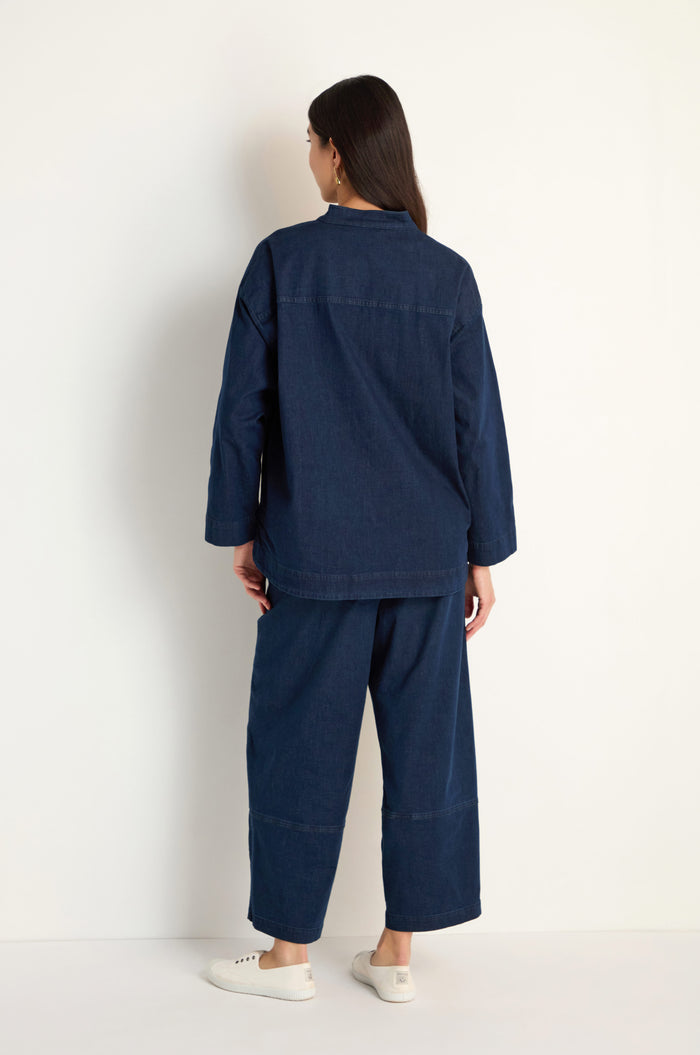 A person stands facing away, wearing the Stretch Denim Boxy Jacket in dark blue with matching wide-leg pants and white sneakers, set against a plain light background.