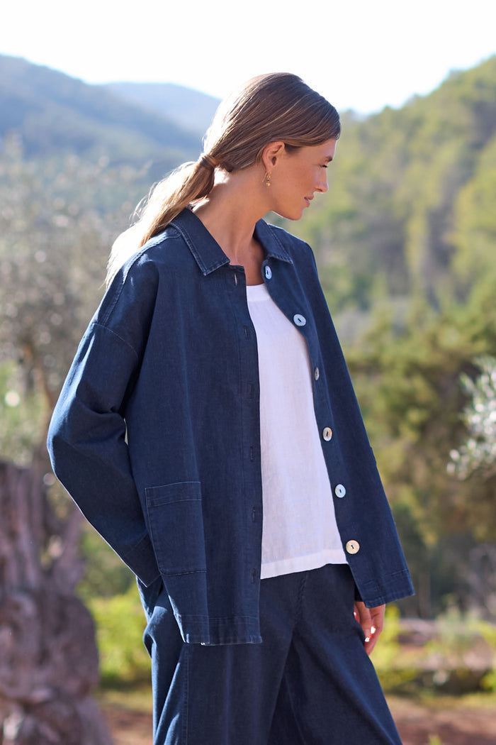 Beneath a sunny sky and surrounded by trees, a person sports the Stretch Denim Jacket and pants in a classic denim ensemble, effortlessly styled with a crisp white shirt underneath.