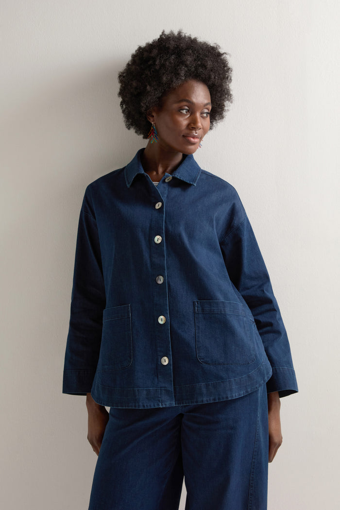 A person models the art of layering by wearing a Stretch Denim Jacket with a boxy silhouette, large buttons, and matching pants against a plain background.
