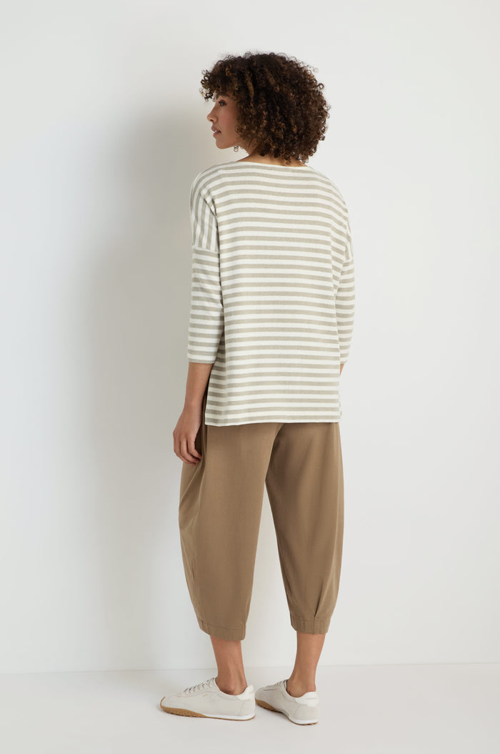 Person stands with back to camera, wearing the Stripe Flared Fleece Top in light gray and white stripes with a relaxed flared silhouette, tan cropped pants, and white sneakers against a plain white background.