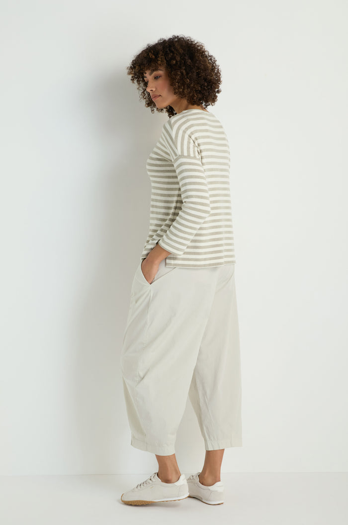 A person stands sideways against a plain background, wearing the Stripe Pocket Fleece Top in beige and white stripes, paired with loose light-colored pants and white sneakers.