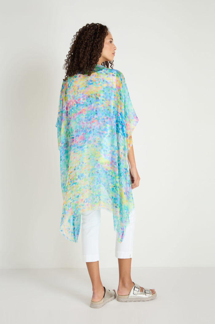 A woman faces away, wearing the Summer Confetti Burst Kimono over white pants and silver sandals against a plain light background.
