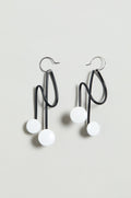 The Symphony Earrings are black wire statement pieces with abstract wavy shapes and two white circular accents each, shown on a light gray background—an ideal choice for contemporary jewellery lovers.