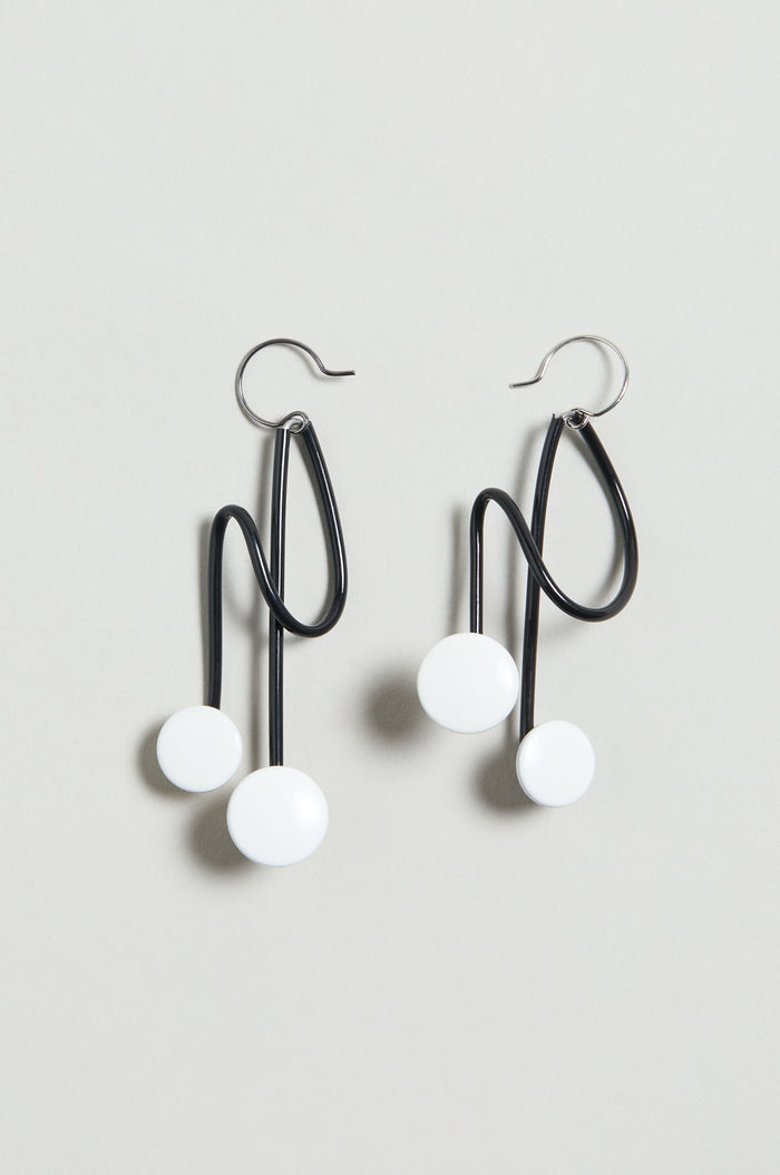 The Symphony Earrings are black wire statement pieces with abstract wavy shapes and two white circular accents each, shown on a light gray background—an ideal choice for contemporary jewellery lovers.
