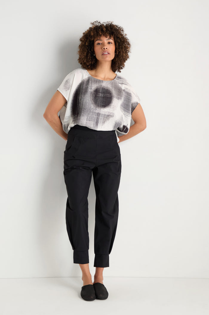 A person wearing black Tapered Cuff Trousers with a flap pocket has their left hand in the pocket; only their lower torso and part of an abstract-patterned shirt are visible.