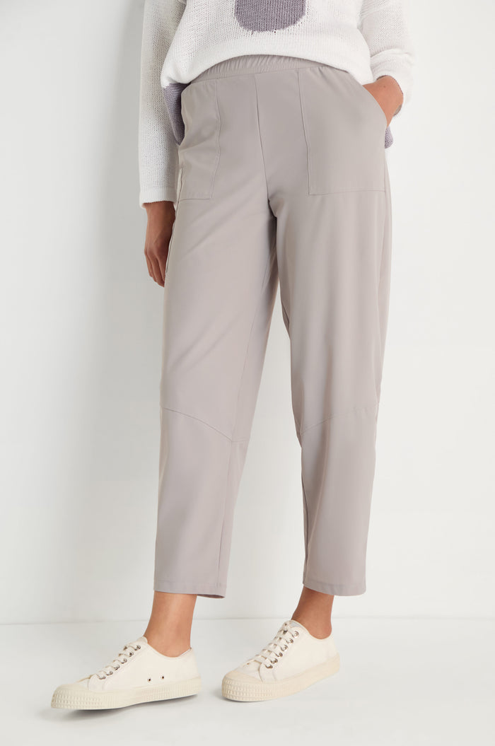 Wearing light taupe Tapered Trousers with front patch pockets and a cropped length, styled with white casual sneakers and a white sweater featuring a light purple design for a modern, relaxed look.