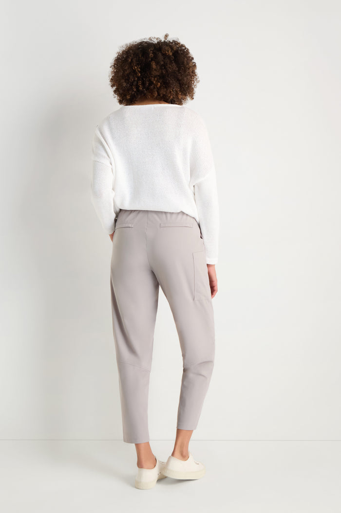 A person stands with their back to the camera, wearing a white long-sleeve top, Tapered Trousers in light gray with a cropped length, and white shoes against a plain white background.