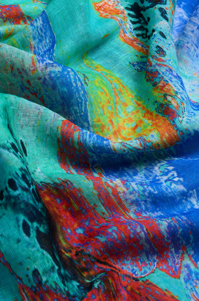 A close-up of the Terra Mare Cotton Linen Scarf highlights its colorful abstract print in blue, green, yellow, red, and black with soft folds and a textured surface.