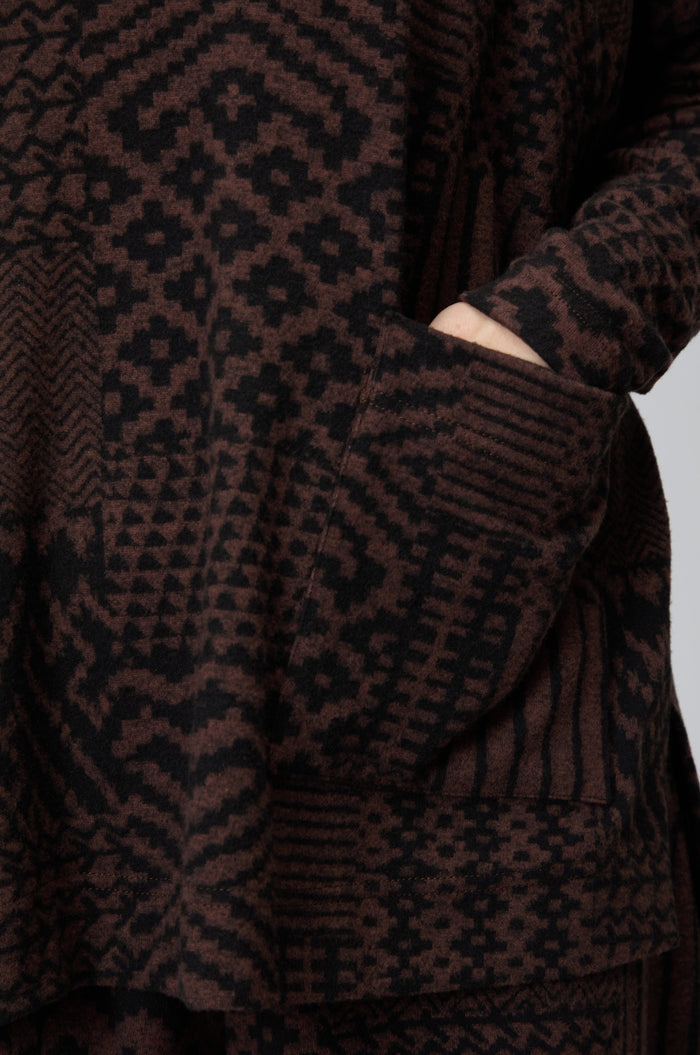 Close-up of a person’s hand in the pocket of a Textured Ikat Patchwork Jersey Top featuring an oversized boxy fit and brown and black geometric designs.