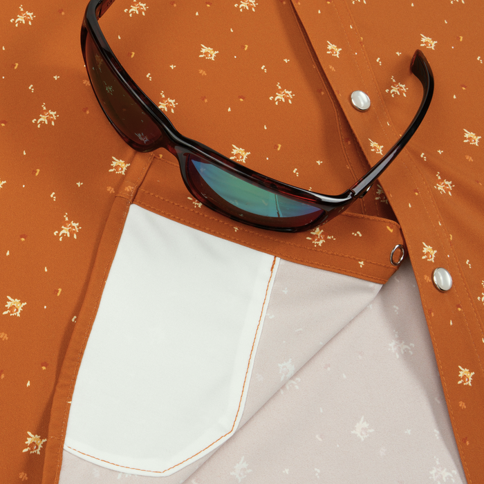 Close-up of rust-colored patterned shirt pocket with sunglasses resting on it, featuring The 5th Year design