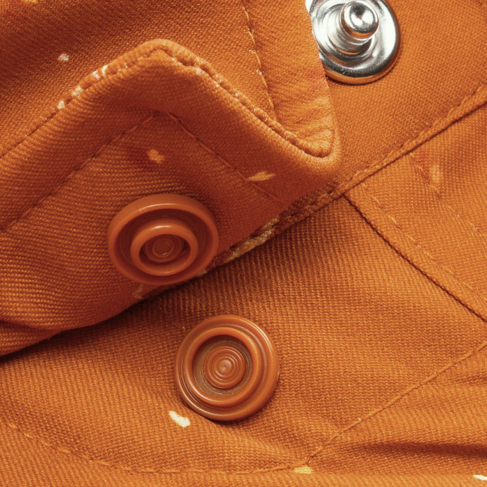 Close-up of orange fabric with snap buttons and small white specks on The 5th Year shirt.