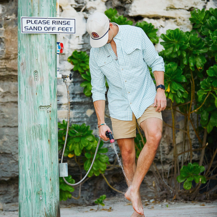 man washes off sand while wearing green and white long sleeve performance shirt
