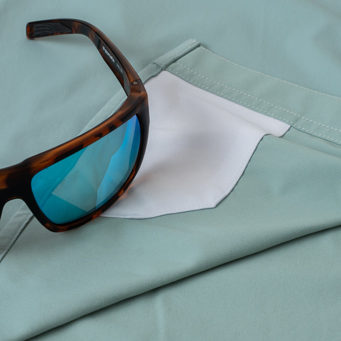 Close-up of The Antilles shirt pocket with tortoiseshell sunglasses resting on light green fabric