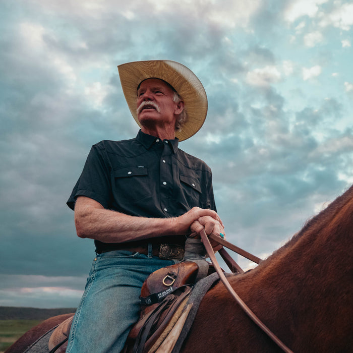 Man wearing The Bandera shirt and cowboy hat riding a horse outdoors