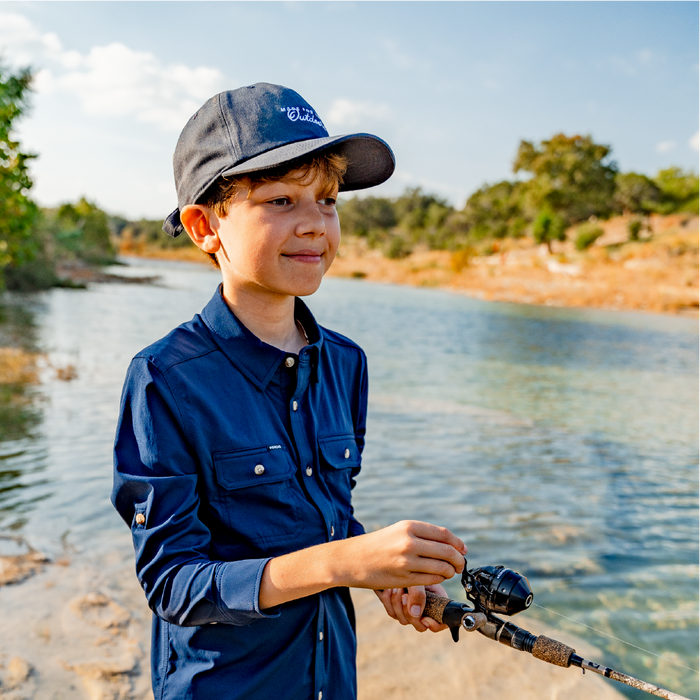 Young boy reeling in a fish wearing navy button down fishing shirt